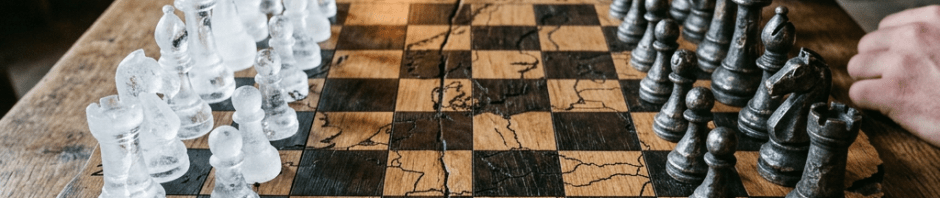 Chessboard with white and black pieces on a carved rustic wooden table with a fireplace in the background