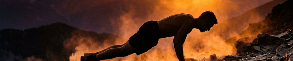 Man performing push-ups on rocky mountain slope at sunset