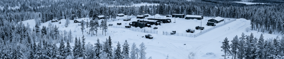 Aerial view of a snowy military outpost surrounded by snow-covered trees under a cloudy sky