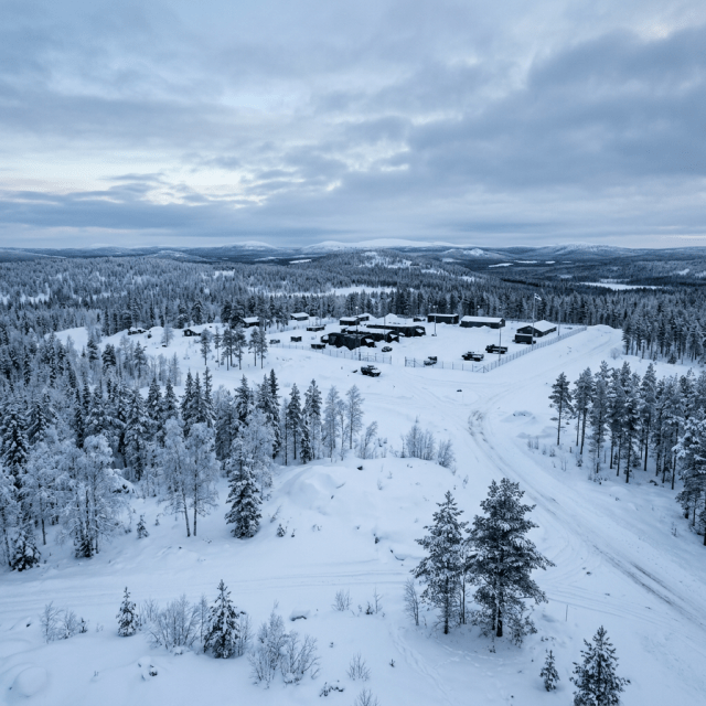 Aerial view of a snowy military outpost surrounded by snow-covered trees under a cloudy sky