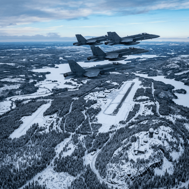 Three fighter jets flying over a snowy airbase and frozen lakes
