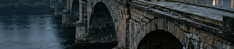 Historic stone bridge crossing a river toward a misty town at dusk